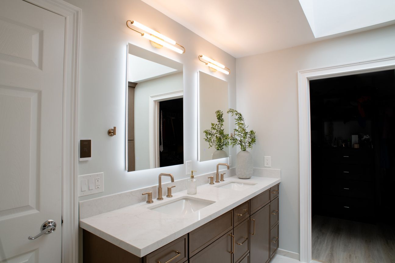 Del Mar primary bathroom remodel with a walnut double vanity, backlit mirrors and brass faucets