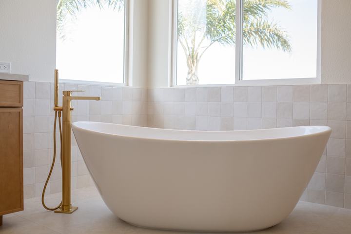 Modern freestanding tub beside floor-mounted brushed-gold filler.