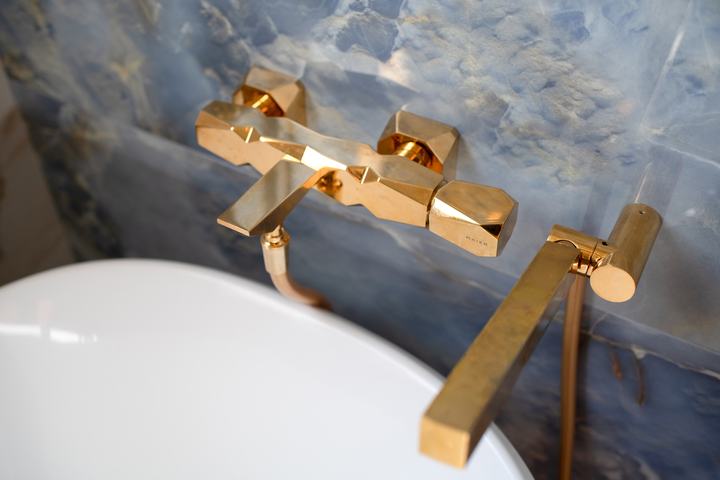 Brass tub filler and handheld sprayer mounted against a blue onyx-look tile wall