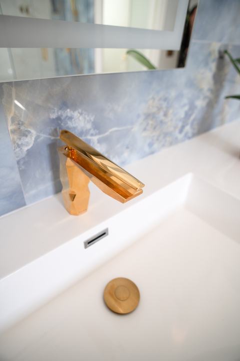Close-up of a brass bathroom faucet over a white countertop and integrated sink
