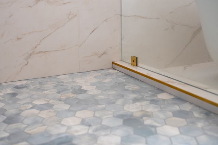 Blue hex mosaic shower floor with glass panel and brass trim detail