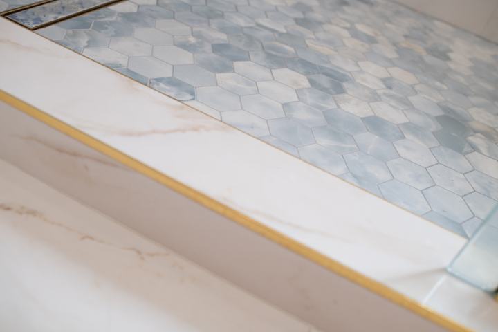 Close-up of shower curb with brass edge and blue hex mosaic tile flooring