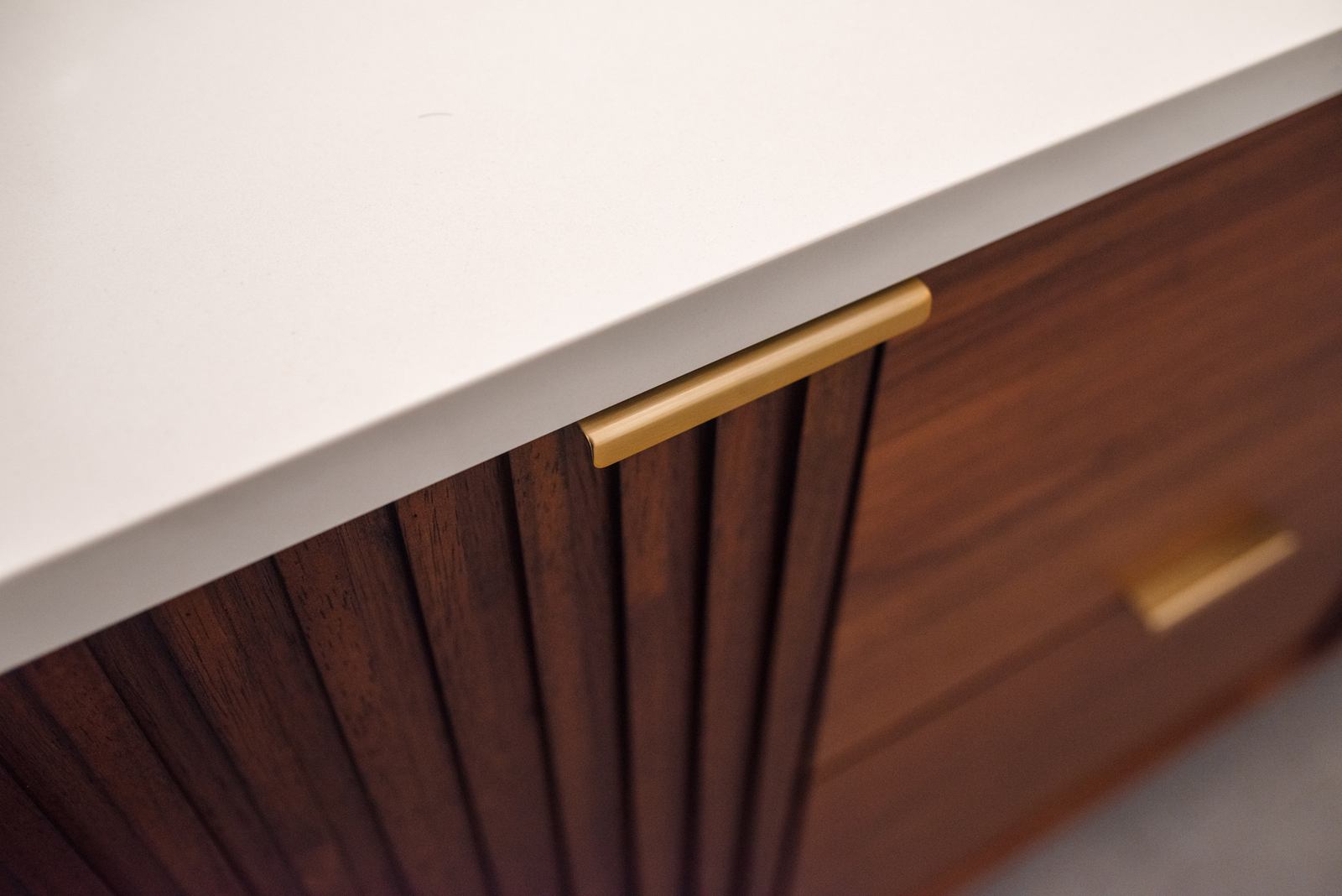 Brass pull and fluted walnut door meeting the white countertop edge