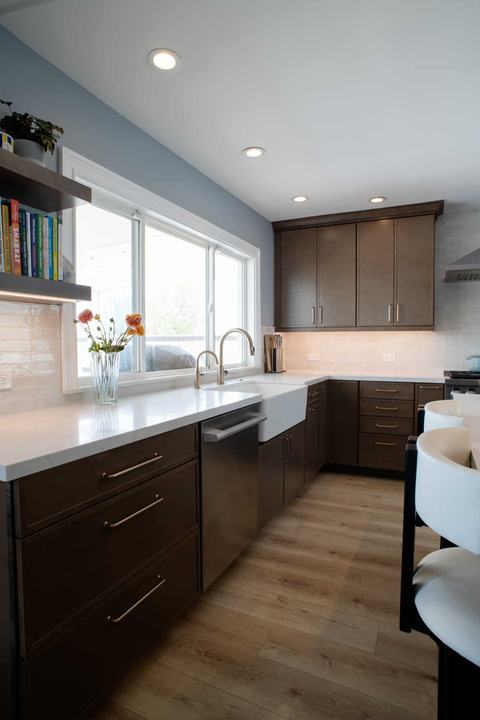 Farmhouse apron-front sink below the window with floating shelves and quartz counters