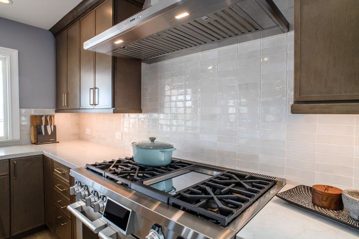 SKS dual fuel range with integrated griddle beneath a stainless hood and glossy ceramic backsplash