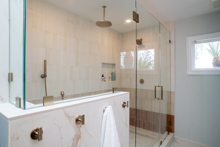 Walk-in shower behind a pony wall capped in Calacatta Oro porcelain, frameless glass above