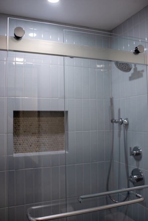 Bypass shower door on its track, niche and chrome controls visible through the glass