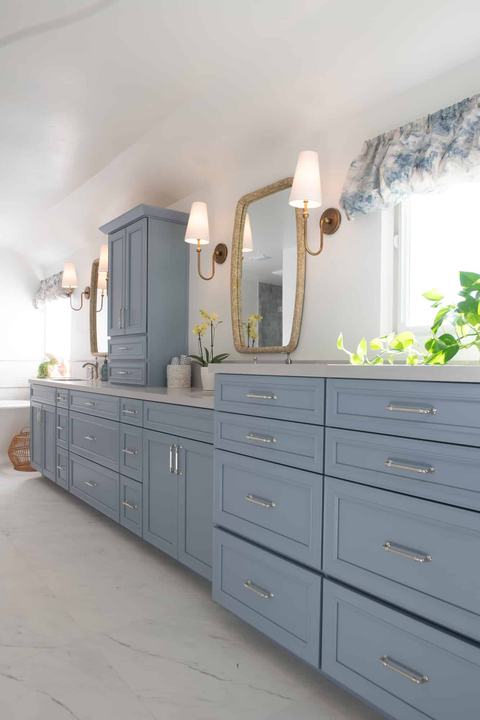 Long blue double-sink vanity with gold sconces, woven-frame mirrors, and quartz countertop