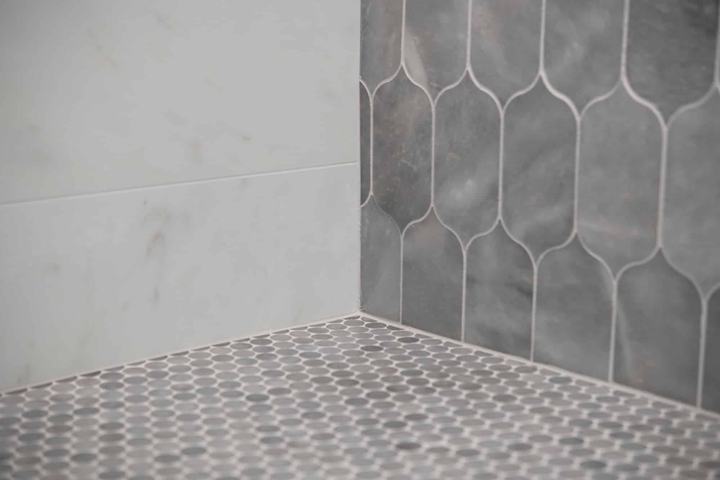 Penny round mosaic shower floor detail with marble-look wall tile and lotus accent tile