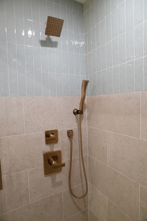 Square showerhead above a handheld wand, both in bronze, where the blue and beige tiles meet