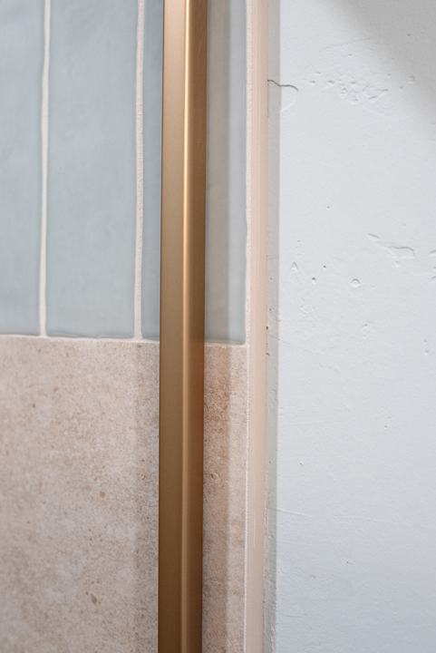 Bronze door channel running down the shower wall beside the tile edge and textured drywall