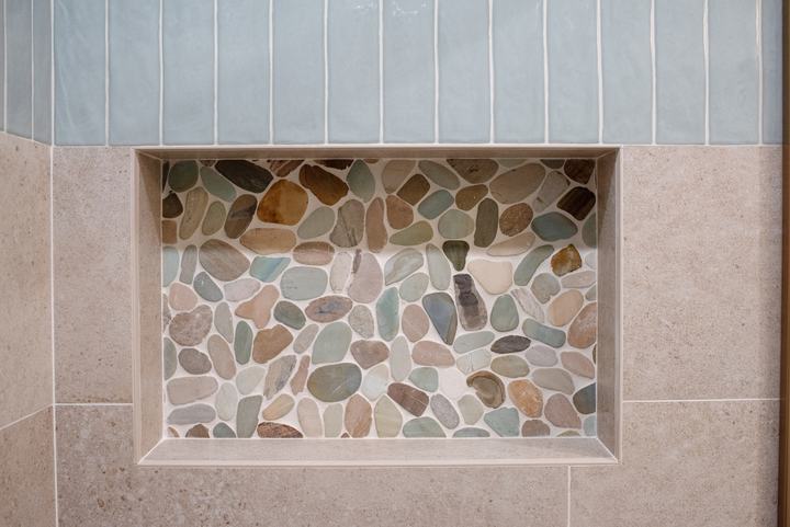 Recessed shower niche lined with multicolored pebble mosaic, its top edge at the tile change