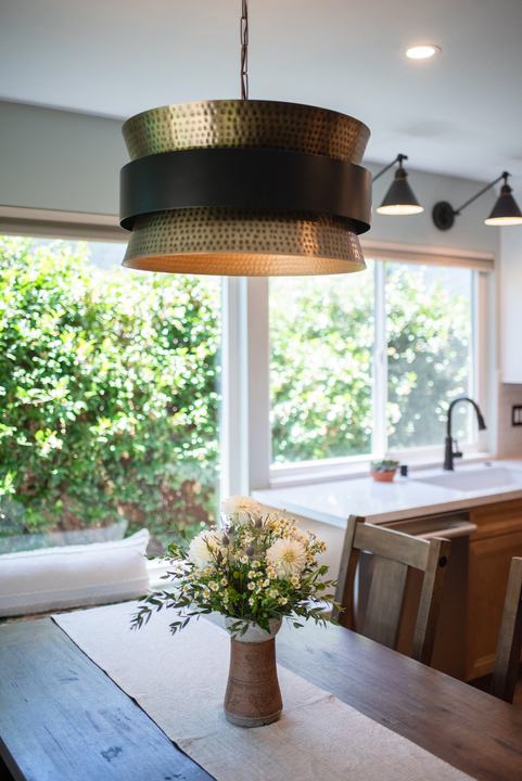 Hammered metal pendant above the table with flowers, sink and window beyond
