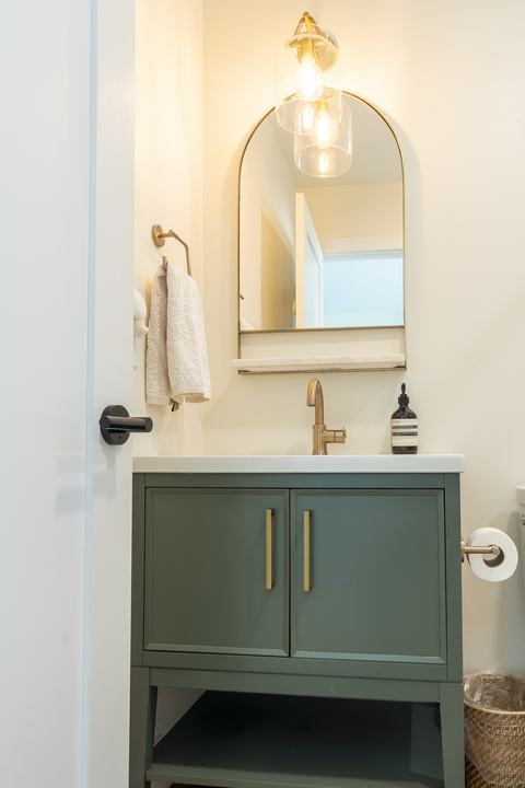 Guest bath vanity in green with brass sconce and arched mirror