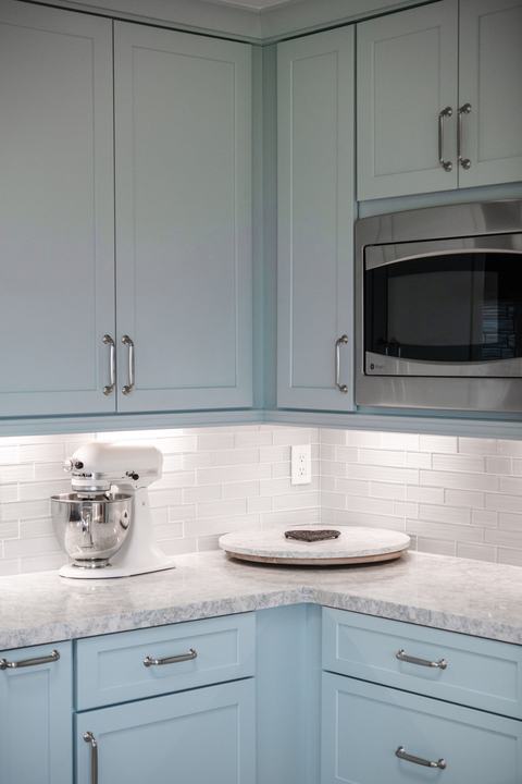 Corner countertop with small appliance storage beneath blue cabinets and built-in microwave