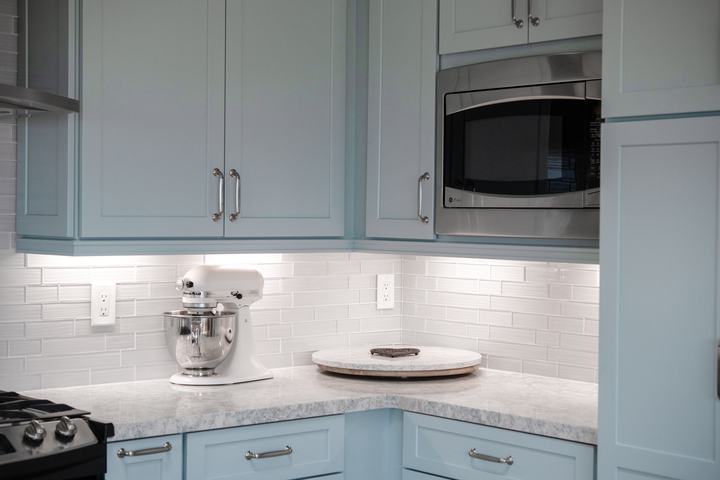 Corner kitchen counter view with mosaic backsplash, quartz surface, and custom blue cabinetry