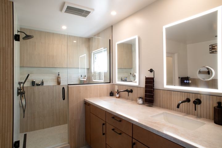 Double vanity with lighted mirrors beside a glass-enclosed walk-in shower