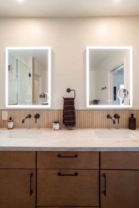 Two lighted mirrors above wall-mounted faucets and a slat tile backsplash