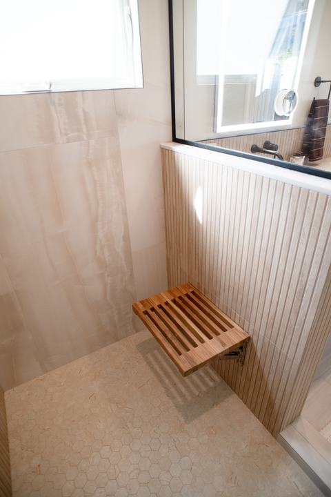 Fold-down teak shower seat above a hexagon mosaic shower floor