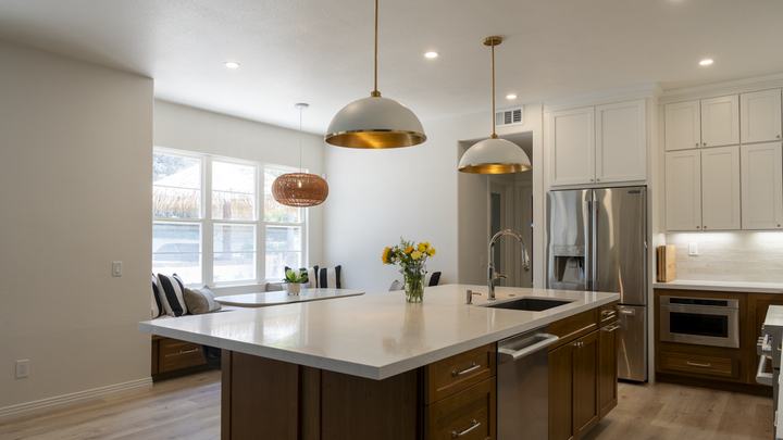 Island sink view toward breakfast nook; quartz surfaces, brass pendant lights, stainless fridge, and light plank flooring