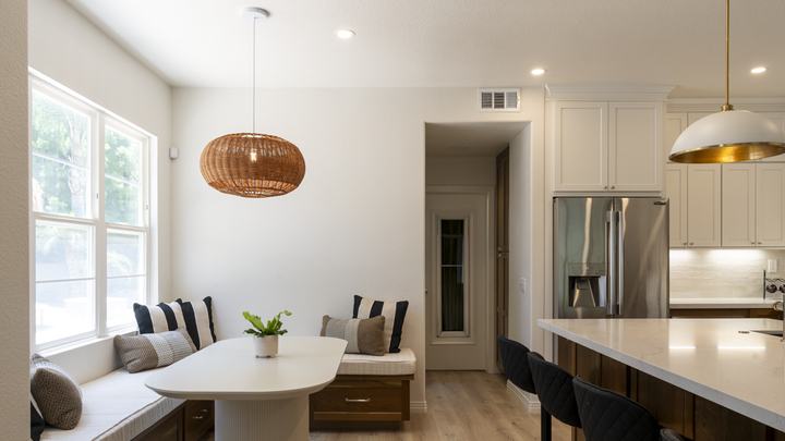 Window banquette with striped pillows, fluted pedestal table, woven rattan light, and glimpse of fridge