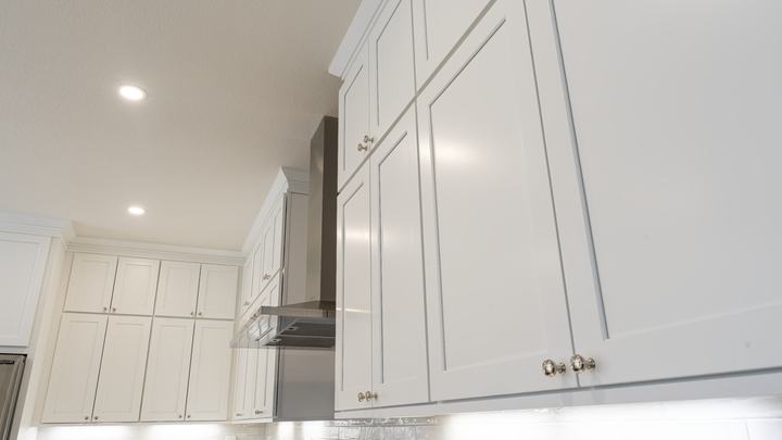 Upward angle of full-height stacked white shaker cabinets flanking stainless range hood and crown trim