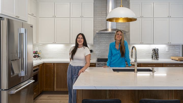 Two Kaminskiy designers standing behind quartz island in completed Poway two-tone kitchen remodel