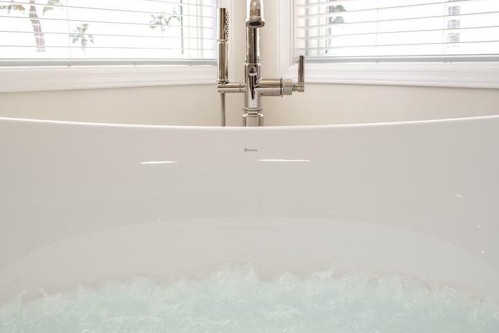 Micro-bubble hydrotherapy churning in the freestanding tub with floor-mount tub filler between corner windows.