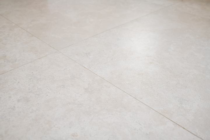 Warm limestone-look porcelain floor tiles in a large-format grid with tight grout joints.
