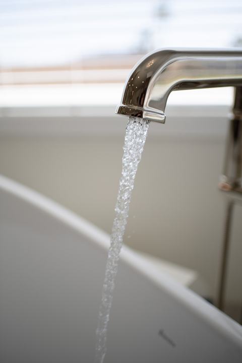 Detail of curved polished-nickel tub spout with streaming water into white freestanding tub