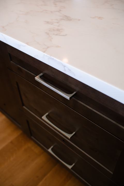 Stained knotty alder island with brushed hardware and white countertop