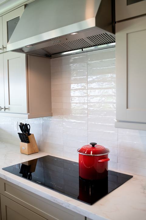 Kitchen induction cooktop, stainless range hood, and glossy white backsplash