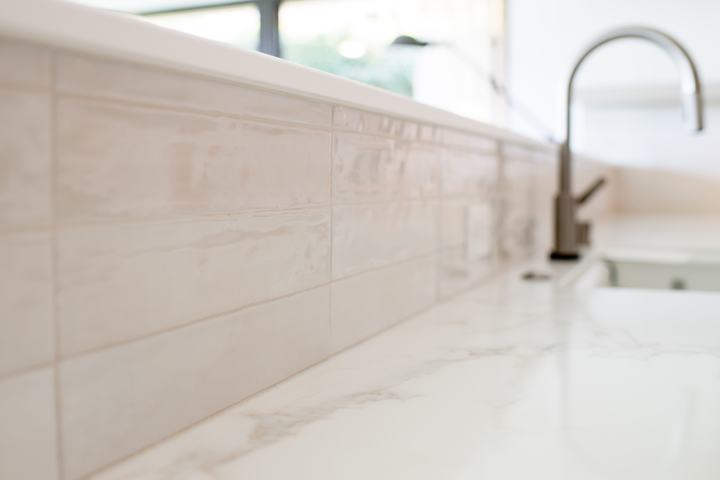 Glossy porcelain backsplash and kitchen faucet detail in remodeled kitchen