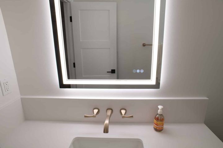 Wall-mounted bath faucet with illuminated mirror and white Silestone countertop