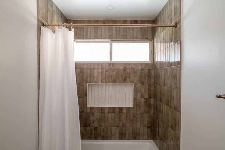 Bathtub and shower with glossy brown porcelain tile and white niche
