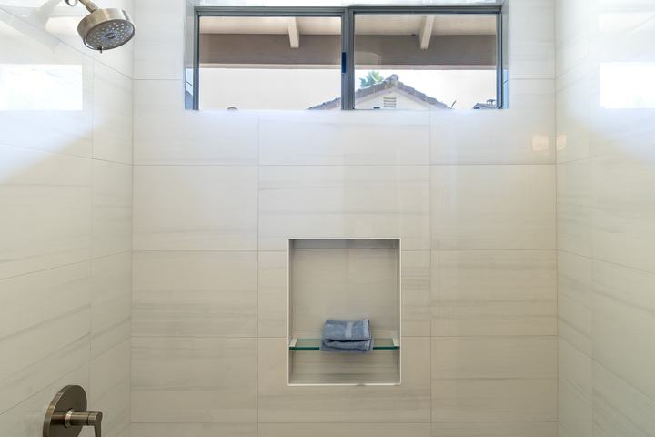 Shower niche with glass shelf centered below a high window in Bianco Lasa wall tile