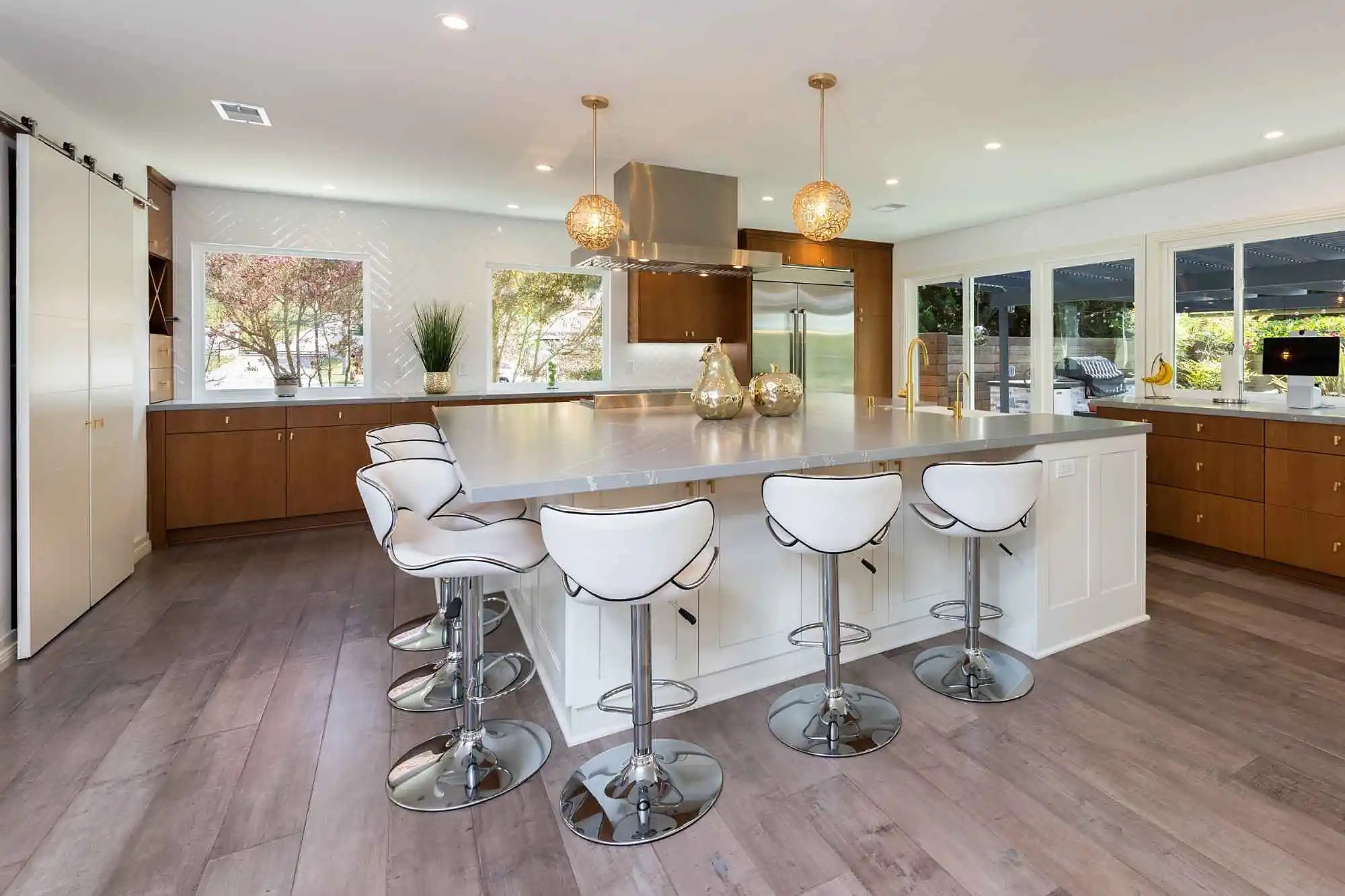 Remodeled San Diego kitchen by Kaminskiy Design and Remodeling with a large white island, walnut cabinets and gold pendants