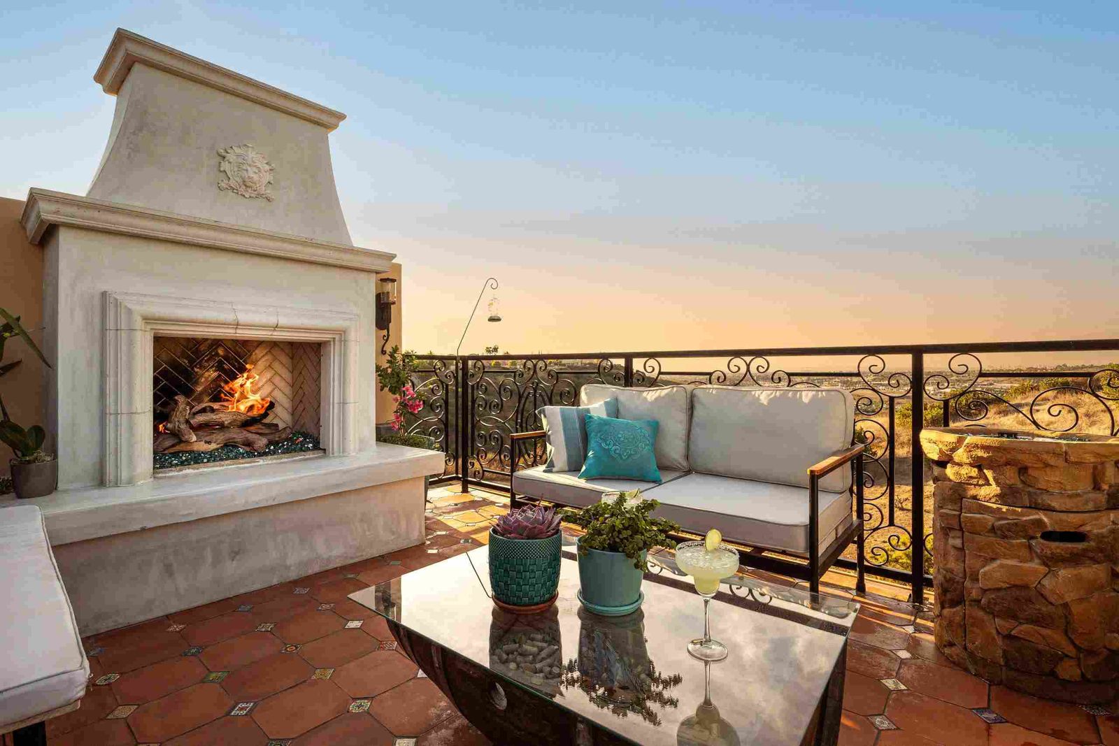 Chula Vista rooftop fireplace in cast stone, lit at sunset beside a white sofa and an iron rail