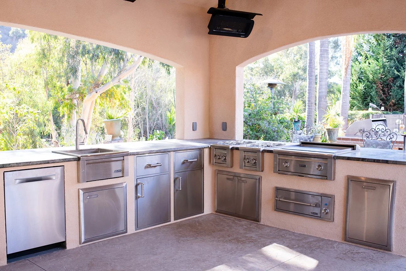 Carmel Valley outdoor kitchen: an L-shaped run of stainless appliances, a stone counter and a sink under a covered patio