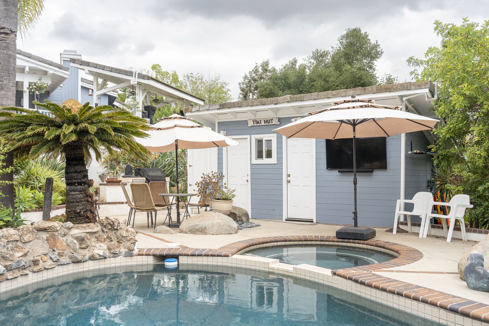 Rancho Bernardo pool with a gray tiki hut pool house, umbrellas and a rock waterfall