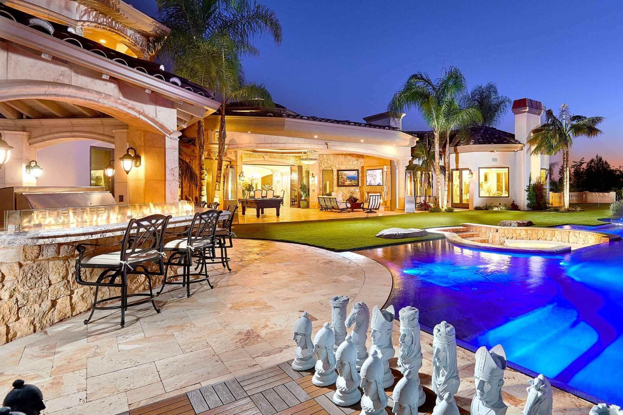 A San Diego backyard at dusk after its Kaminskiy outdoor living remodel: the pool, the lawn and the covered outdoor living room