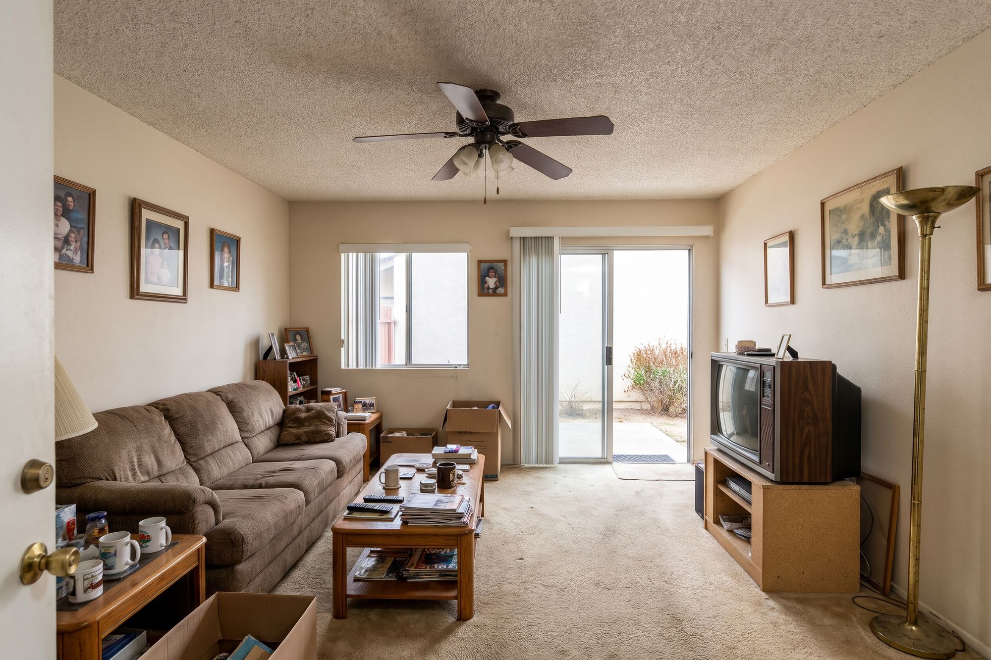 Before: a small lived-in 1980s living room with a low popcorn ceiling, a narrow sliding door to the patio, worn carpet and an old sectional