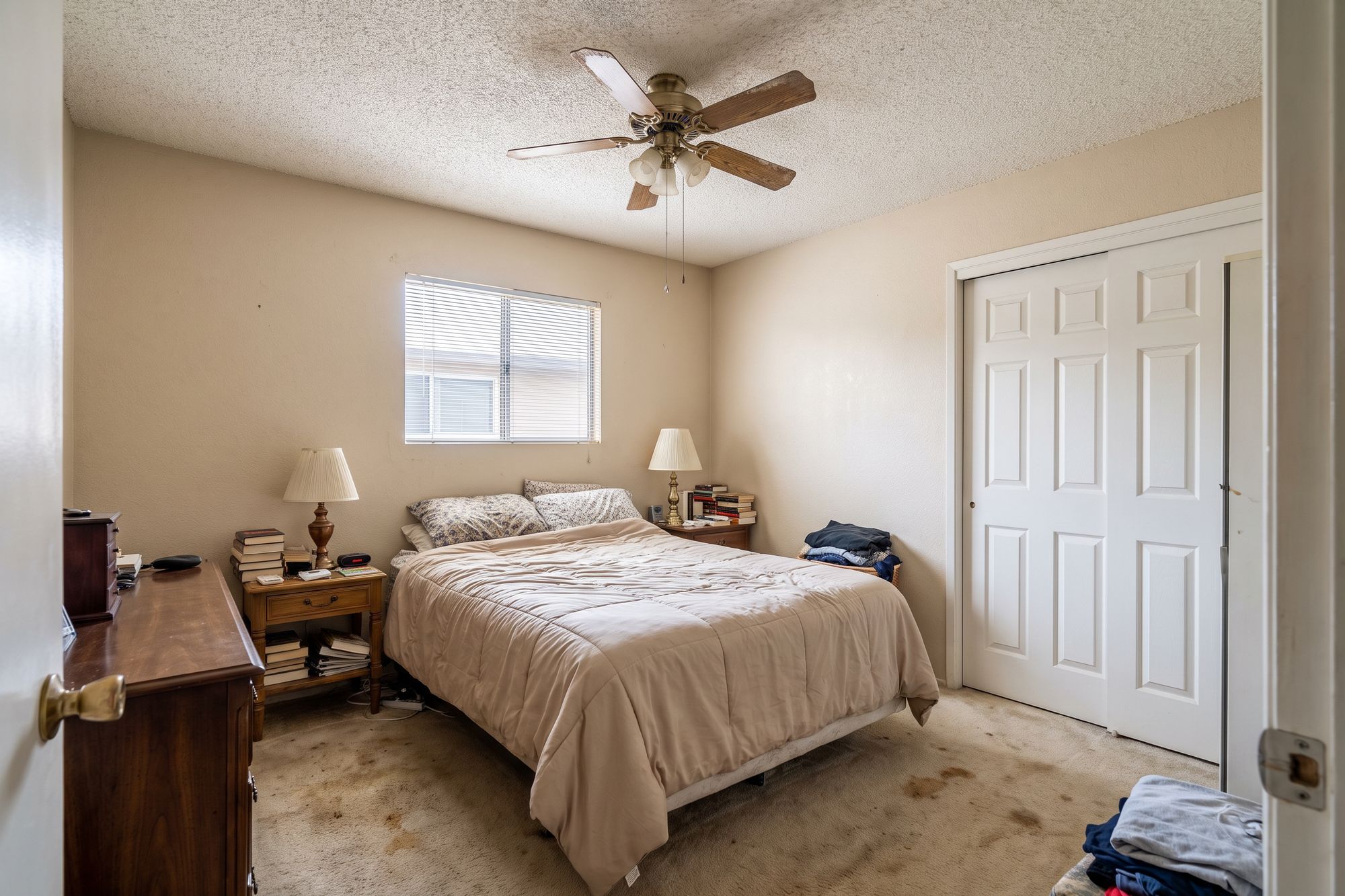 Before: a small lived-in 1970s bedroom with a low ceiling, one small window, bifold closet doors and worn carpet